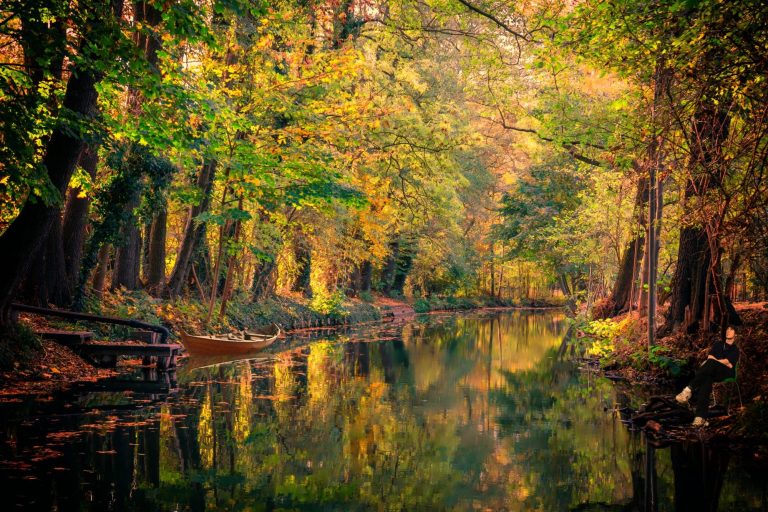 Blick auf einen ruhigen Fluss, umgeben von buntem Herbstlaub und spiegelndem Wasser.