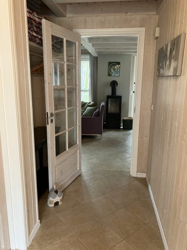 Ein heller Flur mit offener Tür, Blick auf ein Wohnzimmer mit Möbeln und Fenster.