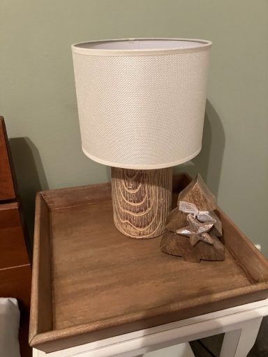 Ein Tischlampen mit beiger Shade und einem dekorativen Holzsockel auf einem Holztablett.