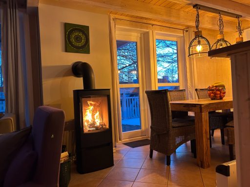 Gemütlicher Wohnraum mit einem Holzofen, einer Essgruppe und Blick auf den Abendhimmel.