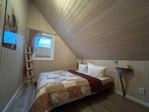 Schlafzimmer mit Dachschräge, Bett mit Kissen und schöner Holzverkleidung.