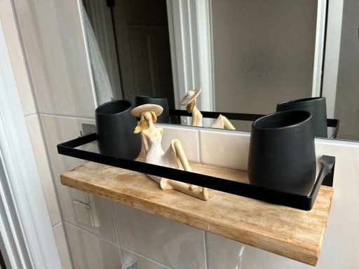Holzregal mit schwarzen Töpfen und einer stylisierten Dekfigur in einem Badezimmer.