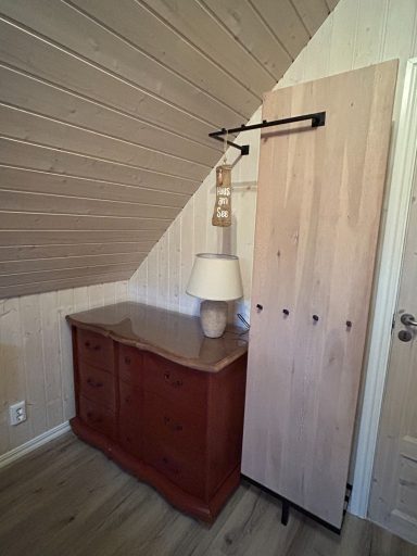 Holzkommode mit Lampe und  Kleiderschrank unter geneigtem Dach.