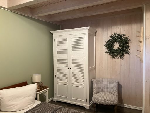 Weißer Schrank in einem Schlafzimmer mit hellgrüner Wand und einem Stuhl.