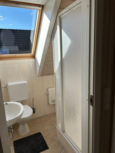 Badezimmer mit Dusche, WC und Fenster unter dem Dach.