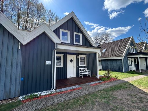 Haus mit blauer Fassade, weißen Fenstern und Veranda, umgeben von Bäumen.
