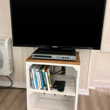 Fernseher auf einem weißen Regal mit DVDs und einer Fernbedienung darunter.