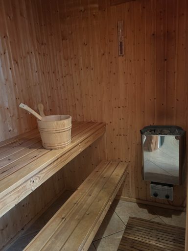 Holzsauna mit Holzschüssel und Ofen, Bänke aus hellem Holz.