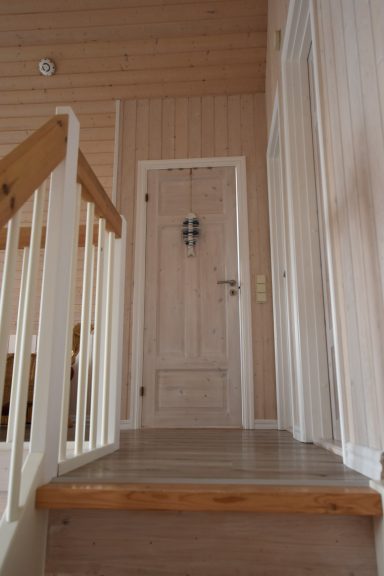 Holztreppe führt zu einer abgeschlossenen, hellen Zimmertür mit Fenster.