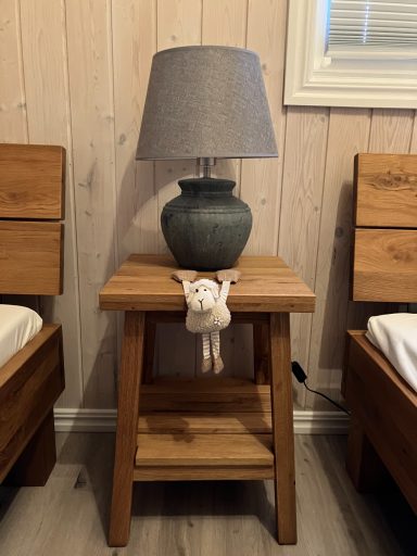 Holztisch mit grauer Lampe und einem kleinen Stofftier auf dem Tisch.