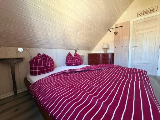 Gemütliches Schlafzimmer mit einem Doppelbett und roten karierten Kissen auf einer Holzdecke.