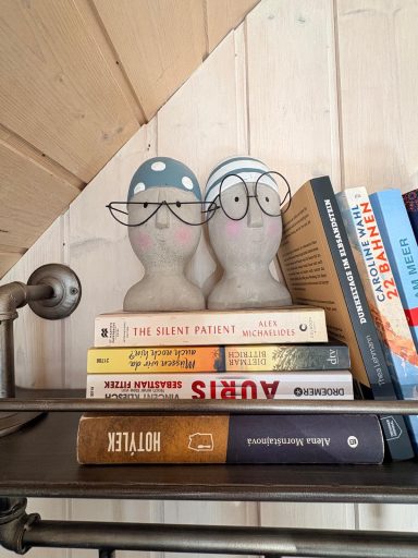 Zwei künstlerische Figuren mit Brille stehen auf einem Bücherstapel.