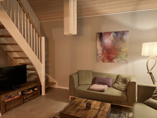 Wohnzimmer mit grünen Sofas, einer Treppe, einem Fernseher und modernen Kunstwerken an der Wand.