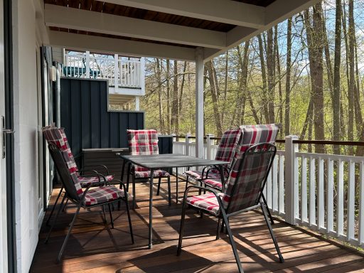 Ein Tisch mit vier gepolsterten Stühlen auf einer verglasten Terrasse im Wald.