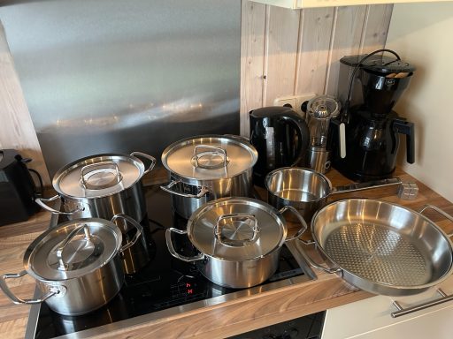 Edelstahlkochgeschirr und Elektrogeräte auf einer Holzoberfläche in einer Küche.