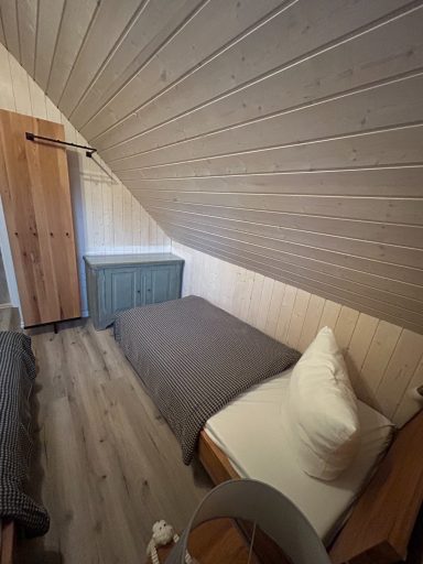 Schlafzimmer mit schrägem Dach, Bett, Kissen und Holzschränken.